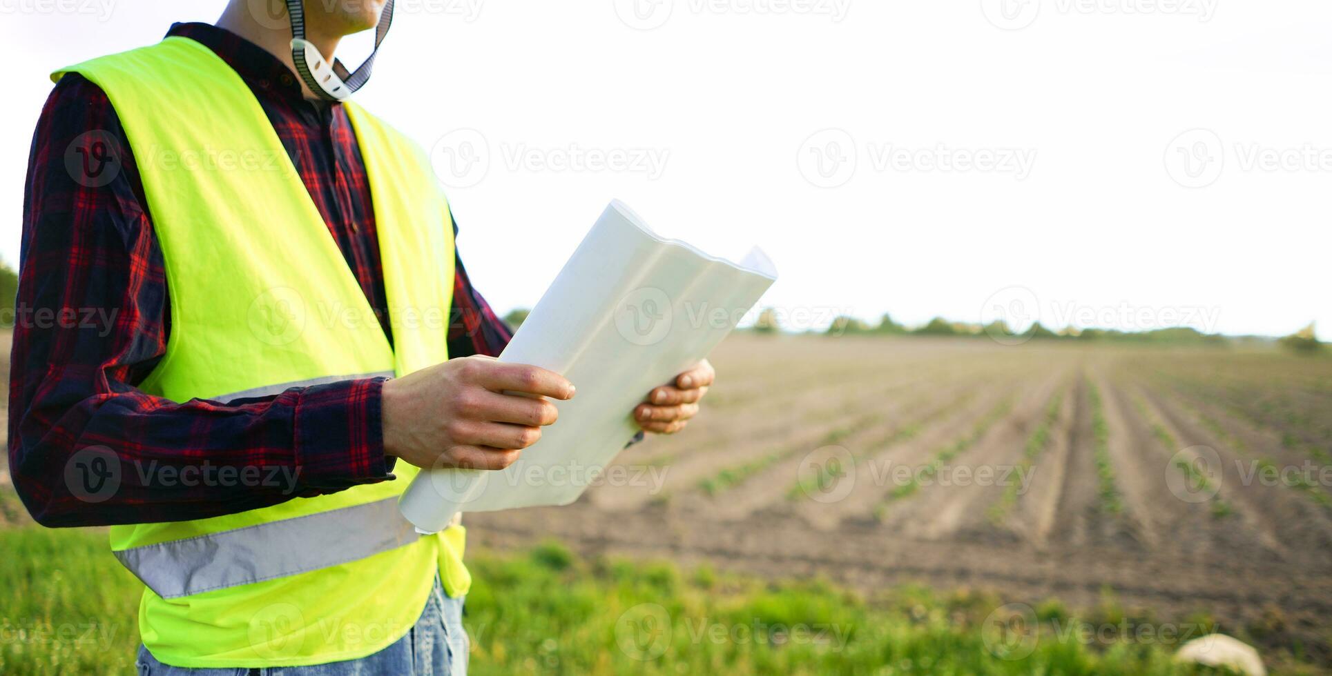 Construction worker holding plan construction plan. Empty field in the background. Occupational Safety and Health OSH photo