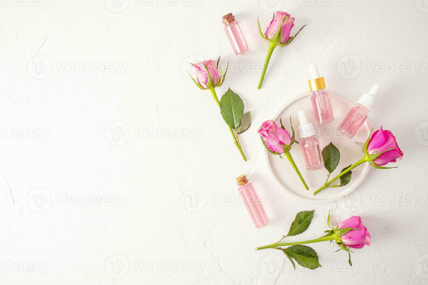 Rosa petróleo y agua en varios vaso botellas en un blanco yeso bandeja entre En Vivo rosas. natural orgánico productos cosméticos para personal cuidado. un Copiar espacio. foto