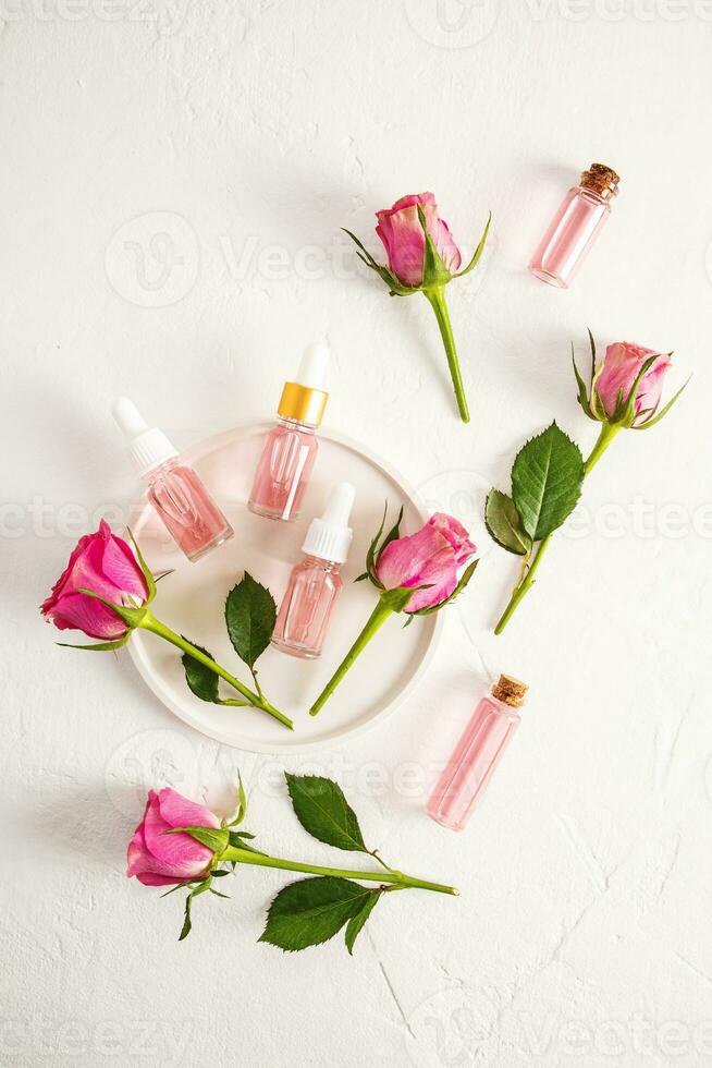 Natural organic facial skin care product based on rose petal oil in cosmetic bottles on a white textured background. Top view. Vertical view. photo