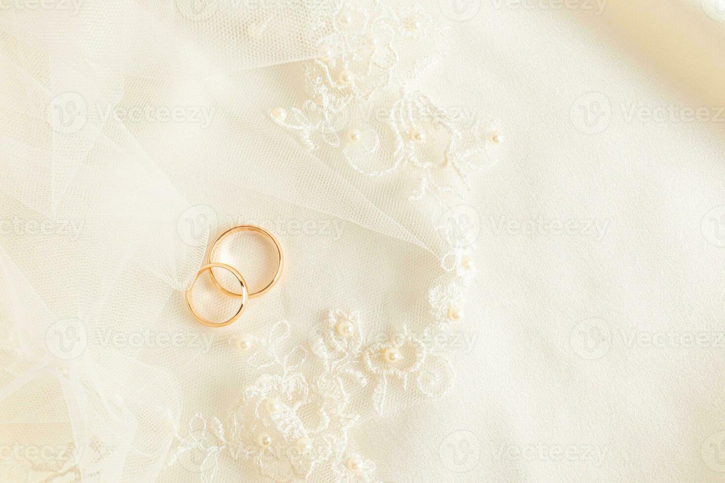 Two gold wedding rings lie on the bride's embroidered tulle with soft pleats. Beautiful wedding background. layout for design. A postcard. photo