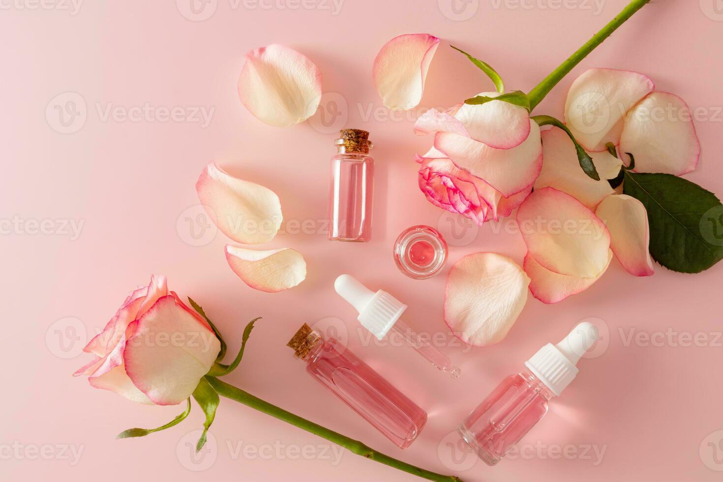 Several different glass cosmetic bottles with serum with rose petal extract and rose water for facial skin care. The top view is flat styling. photo