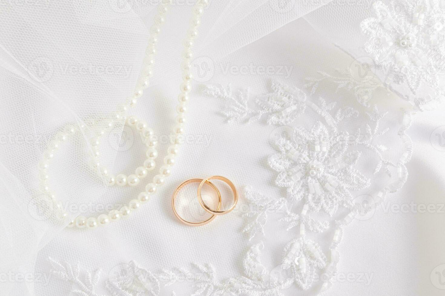 Wedding background with chic white lace part of the bride's veil and two gold wedding rings on it. White pearl beads. Layout of invitations. photo