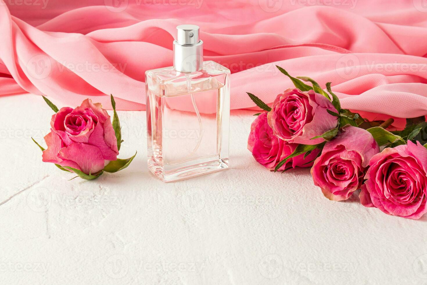 beautiful bottle of women's perfume or eau de parfum against a background of a pink chiffon scarf and fresh roses. Presentation of the fragrance. photo