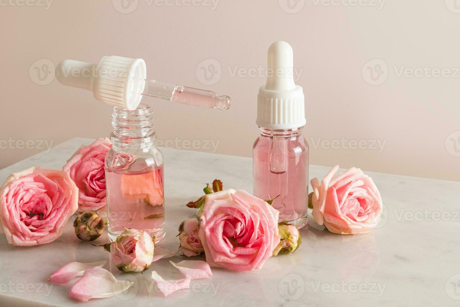 An open bottle of rose oil and a pipette filled with cosmetics on a marble podium with flowers and rose petals. moisturizing, softening the skin. photo