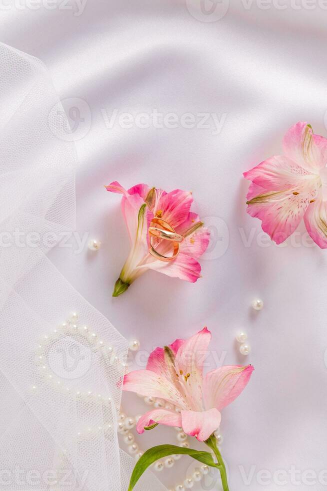 A pair of beautiful gold wedding rings lie in an astromeria flower bud on a white satin background with a piece of veil. postcard. invitation. photo