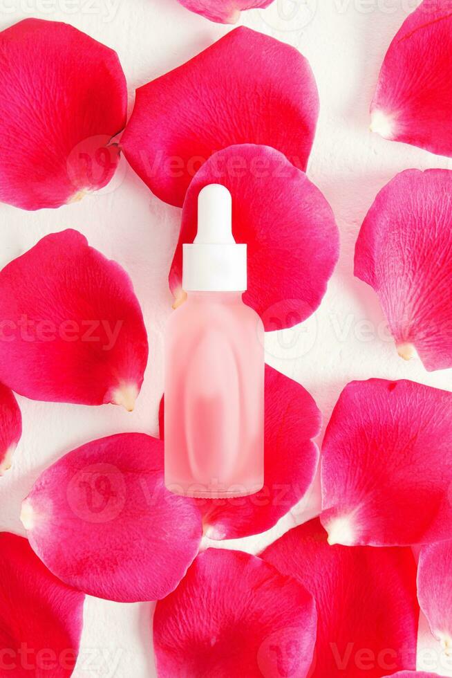 The top view of a white matte bottle with a pipette and a white cap with a natural cosmetic, serum or oil lies on fresh rose petals. photo