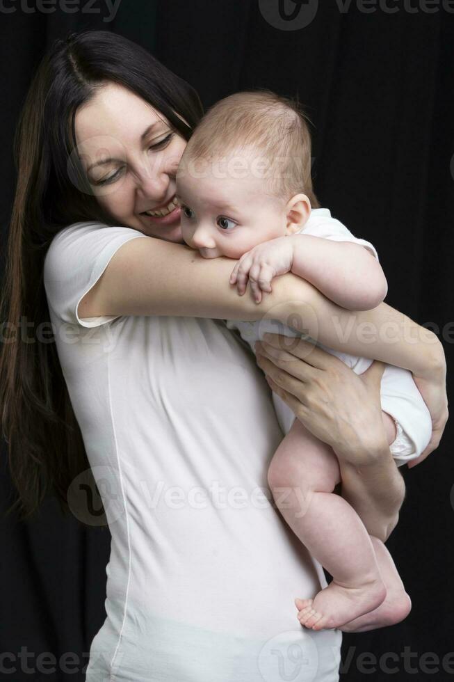 hermosa madre abrazos su bebé. maternidad.mamá y pequeño hijo en un oscuro antecedentes. maternidad. foto