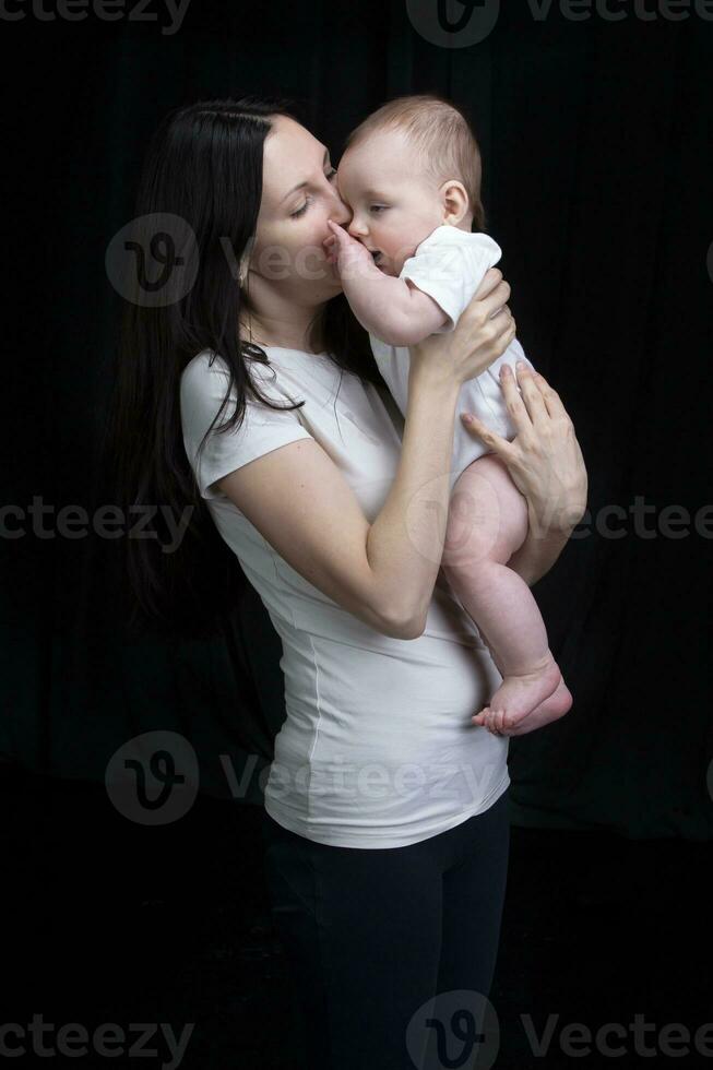 hermosa madre abrazos su bebé. maternidad.mamá y pequeño hijo en un oscuro antecedentes. maternidad. foto