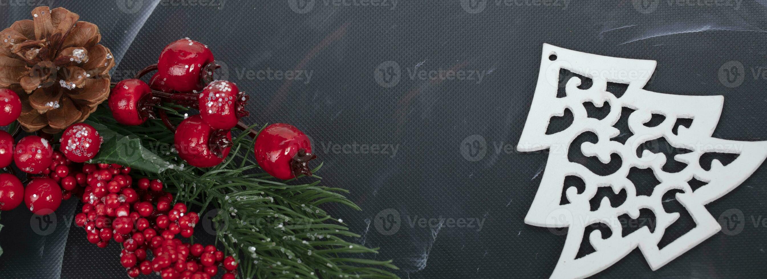 On a black background, a spruce branch with red berries and a pine cone, a Christmas tree. photo