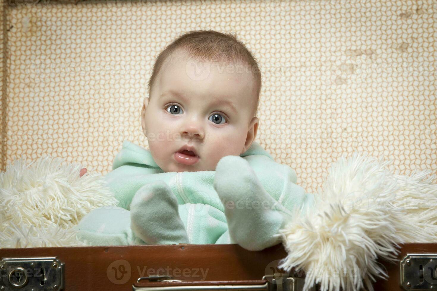 A little kid sits in a retro suitcase and looks at the camera. Funny baby. The boy is four months old. photo