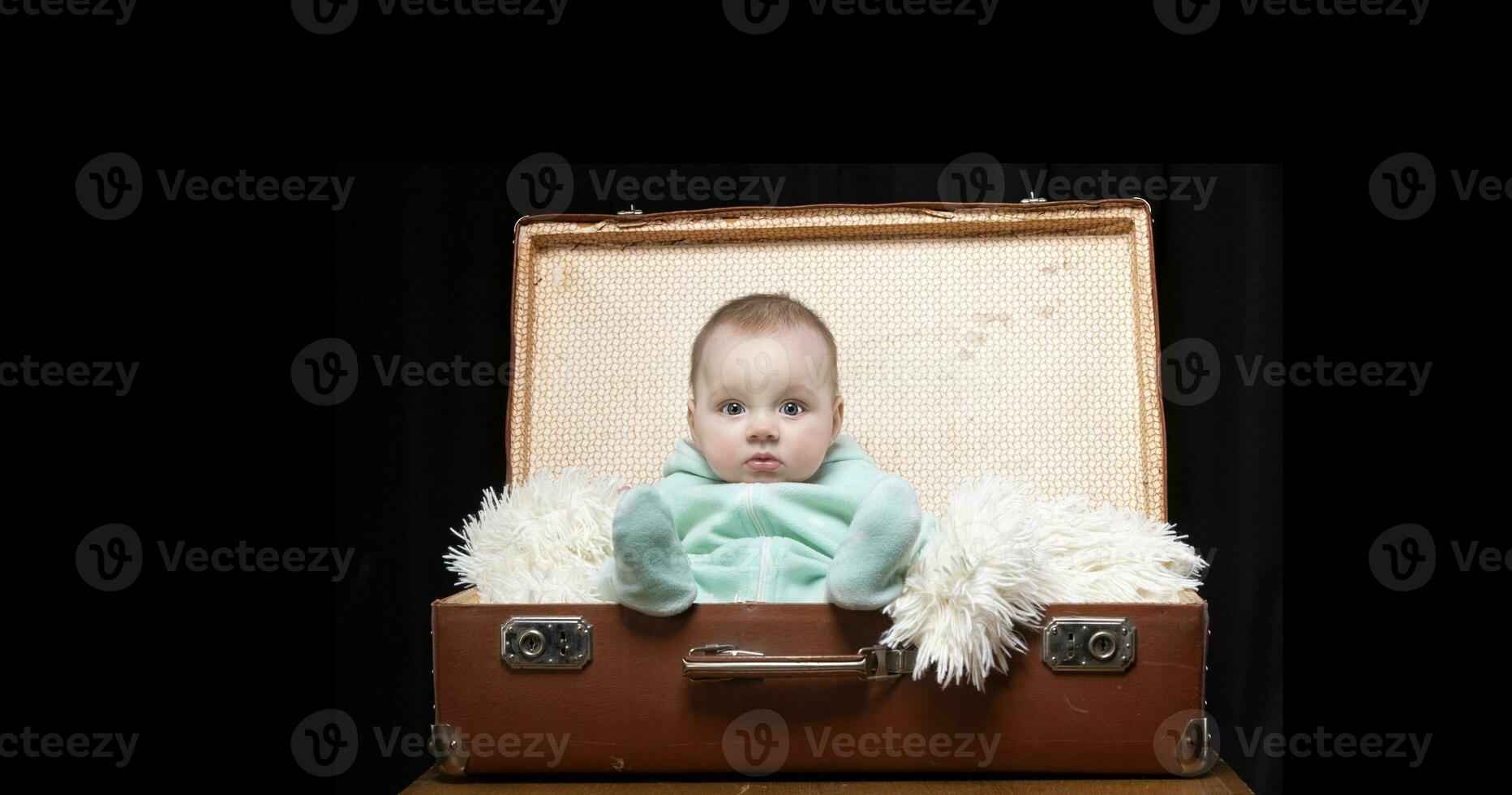 A little kid sits in a retro suitcase and looks at the camera. Funny baby. The boy is four months old. photo