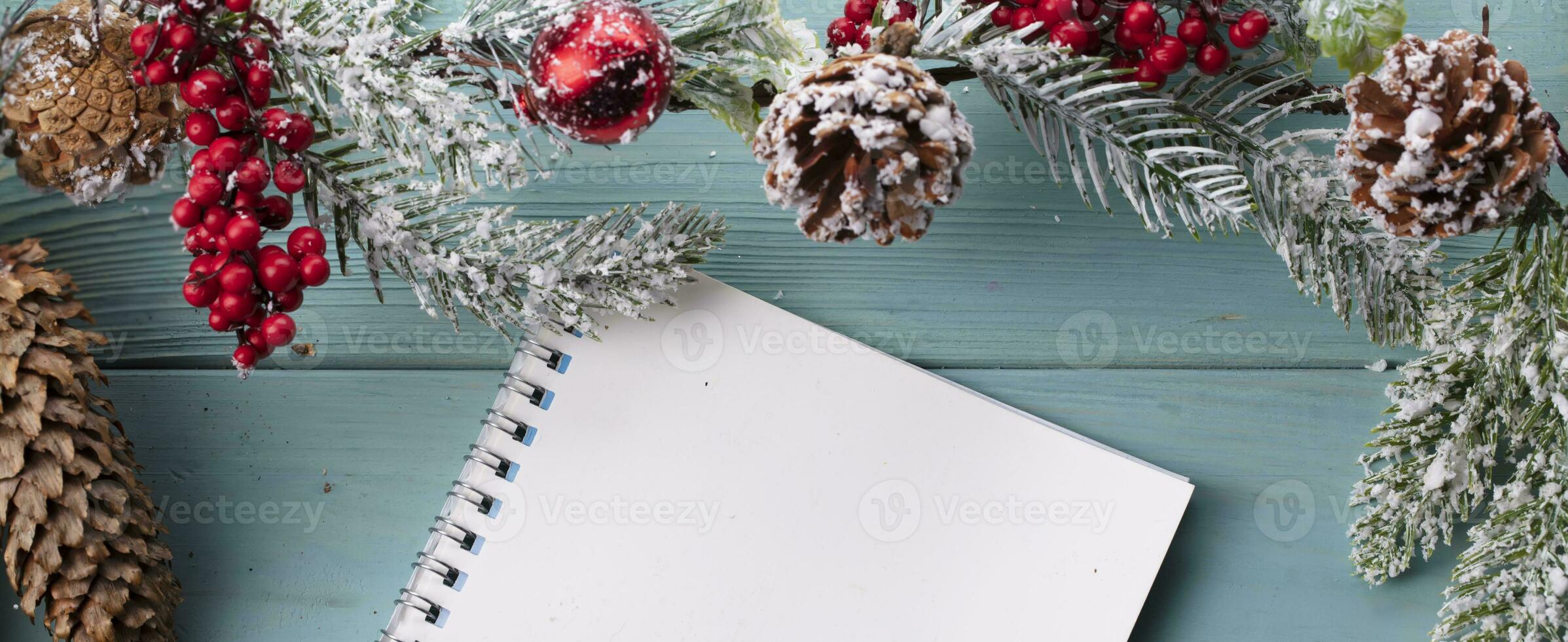 On a turquoise wood background, decoration of a spruce branch, cones and a white sheet from a notebook. Christmas background. photo