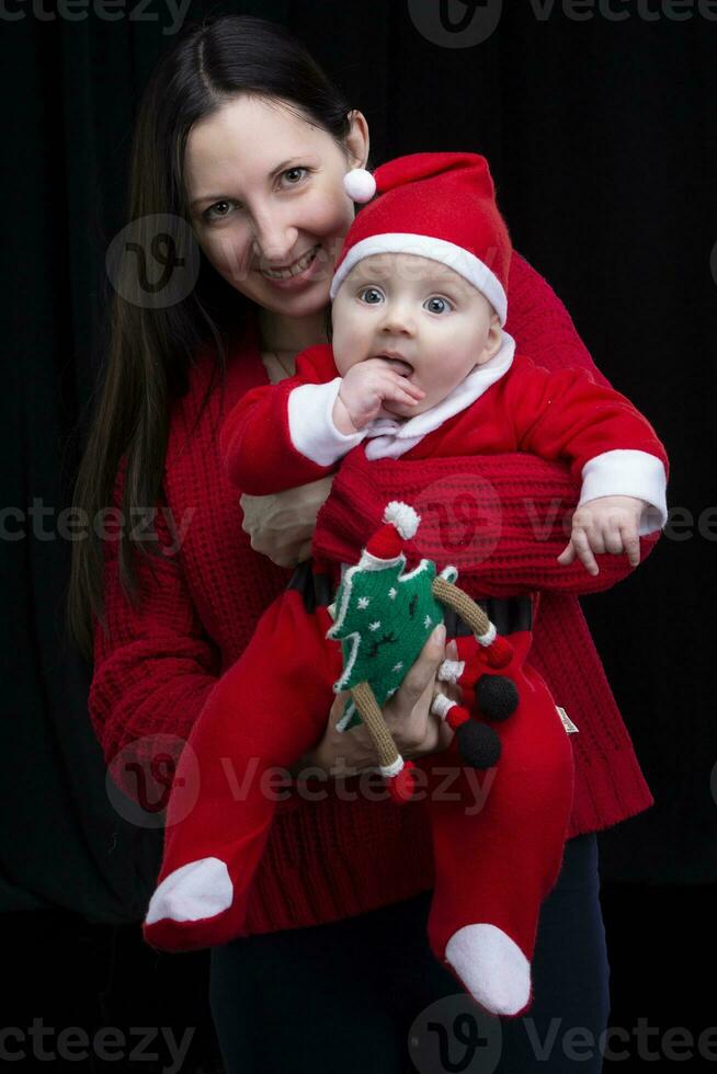 mamá y pequeño niño a Navidad. un mujer sostiene su hijo en su brazos, quien es vestido en Papa Noel claus ropa. foto