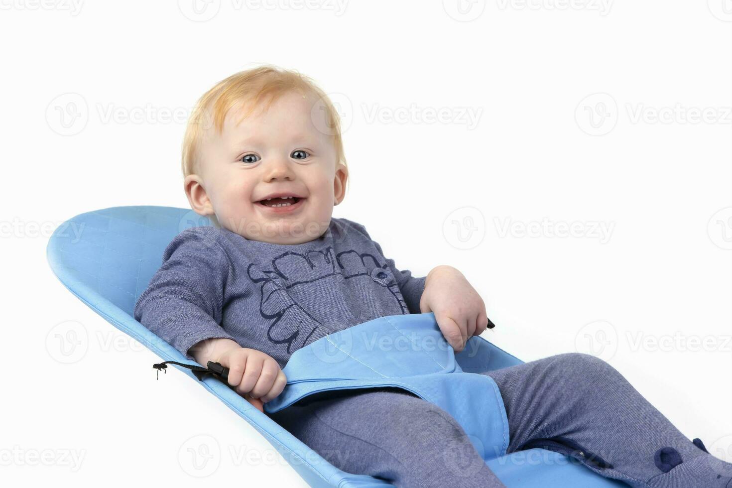 Over white background happy kid in a baby lounger sits and smiles. The boy is one year old. photo