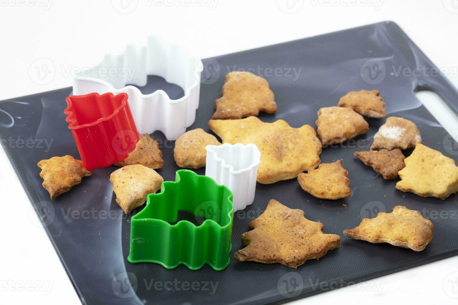 On a cutting board there are Christmas tree-shaped cookies and colored baking dishes. Beautiful Christmas pastries on a white background. photo
