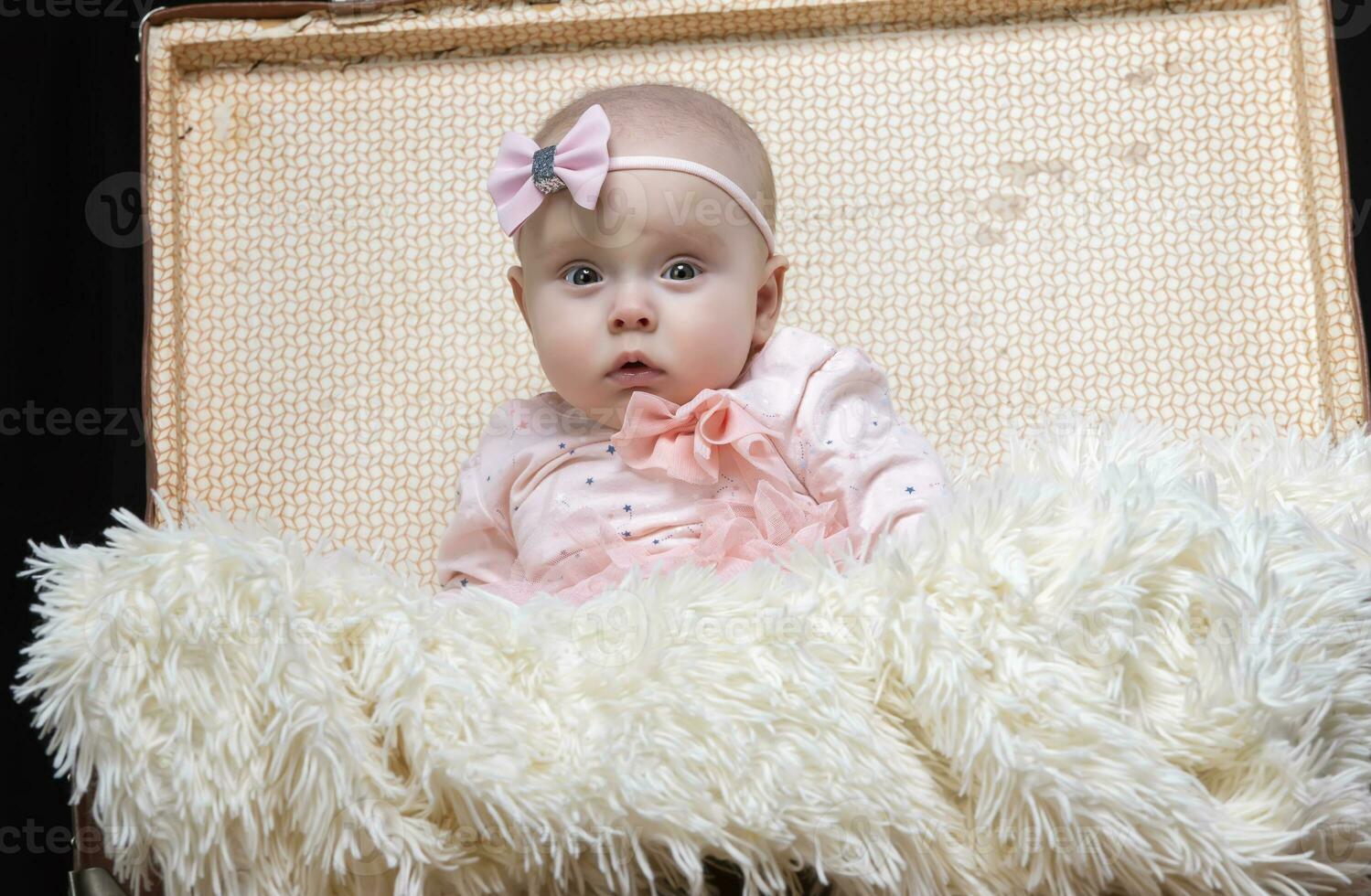 A little baby sits in a retro suitcase and looks at the camera. Pretty Baby. photo