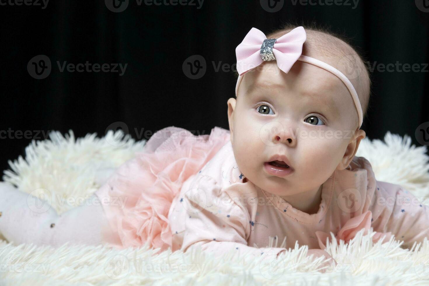 Beautiful baby girl in pink clothes on a black background. Baby at four months old. A funny child. photo