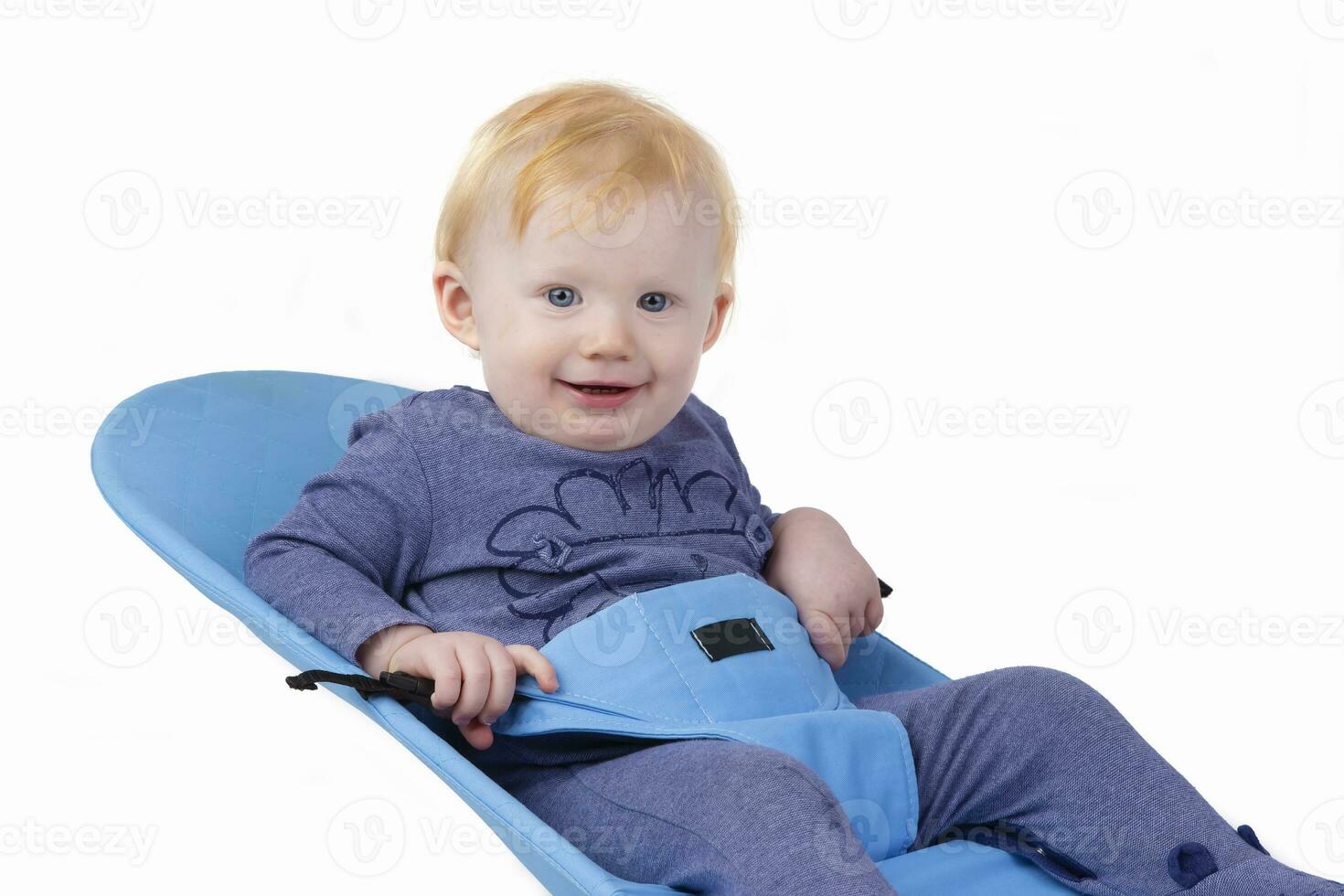 Over white background happy kid in a baby lounger sits and smiles. The boy is one year old. photo