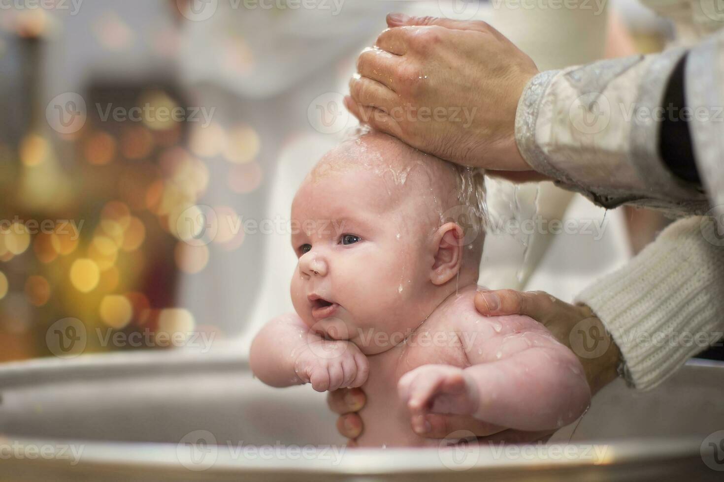 Orthodox baptism of a child.Baby in the baptismal font in the church. The hands of the priest pour water on the child during the ceremony of accepting faith. photo