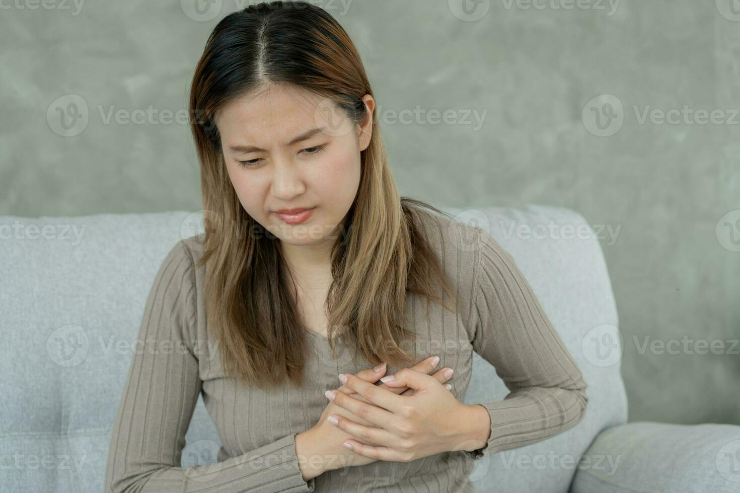 hand hold chest with heart attack symptoms, asian woman have chest pain caused by heart disease, leak, dilatation, enlarged coronary heart, press on the chest with a painful expression photo