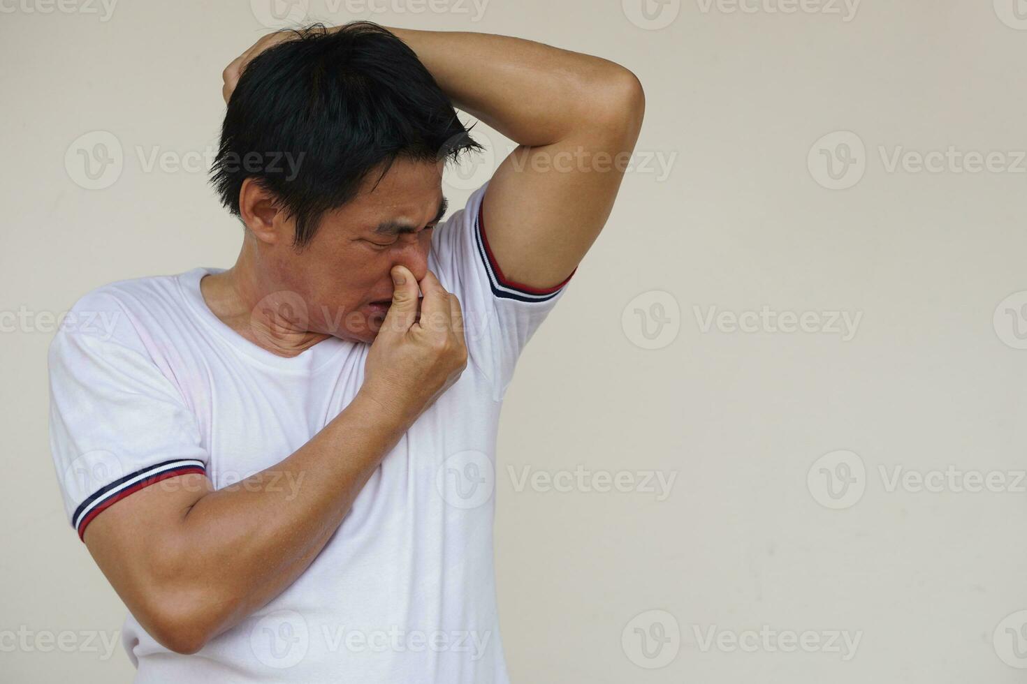 Asian man checks his body odor during he feels hot, raises left arm up, smells his armpit. Close his nose. Concept , health problem. Unpleasant body odor , smell nasty reaction. Negative emotion. photo