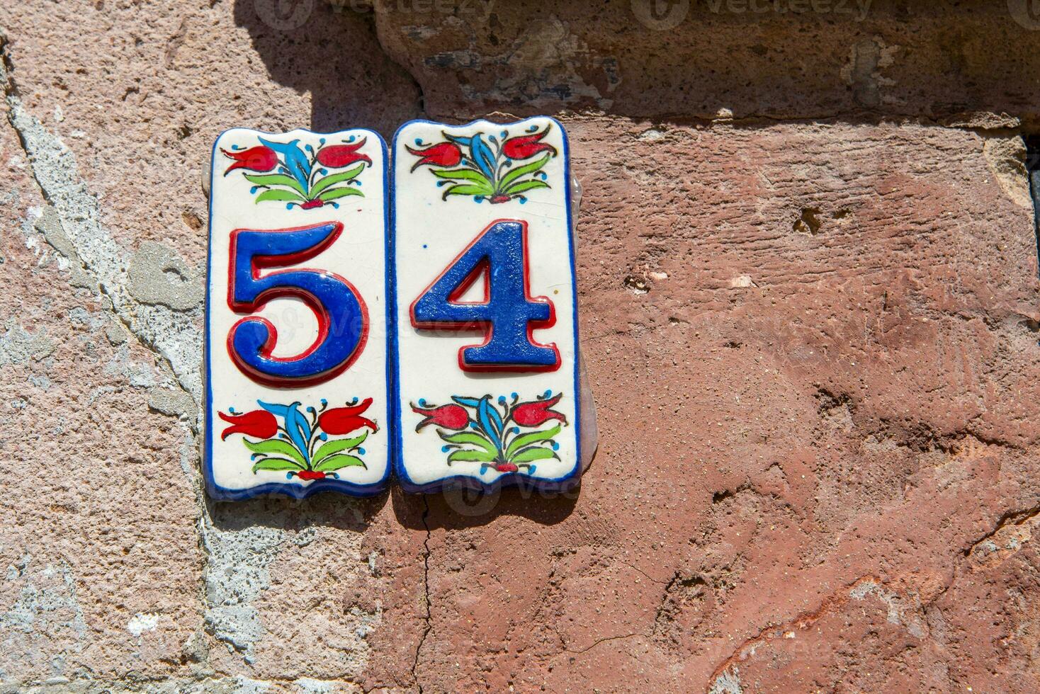 A sign with the number 54 in blue on a pink wall. photo