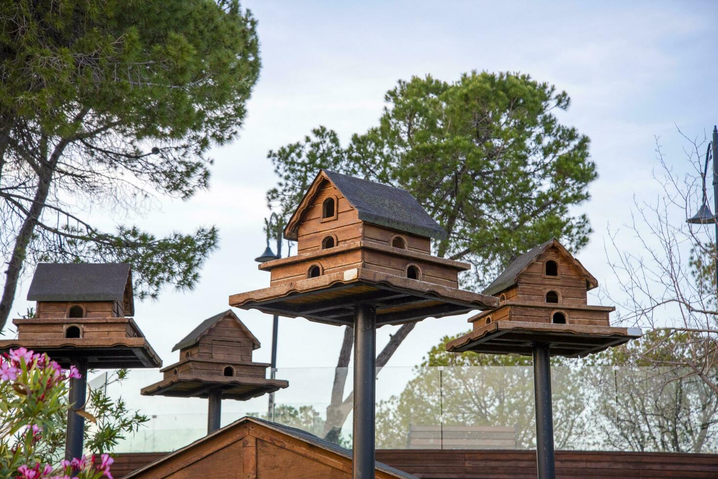 A tiered birdhouse made of wood, painted brown, atop a tall pole with a blue sky in the background. photo