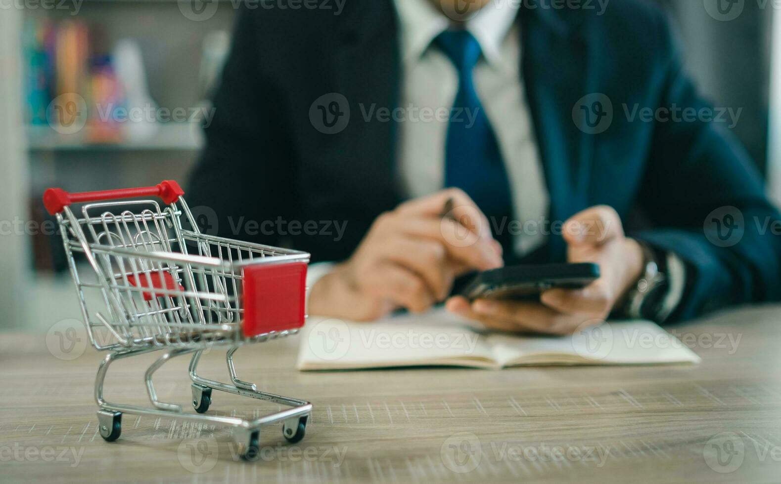 Business man wearing suit and calculates the budget. Shopping cart a on table with mobile. Budget of poor low income family. Rising food and grocery store prices and expensive daily consumer goods. photo