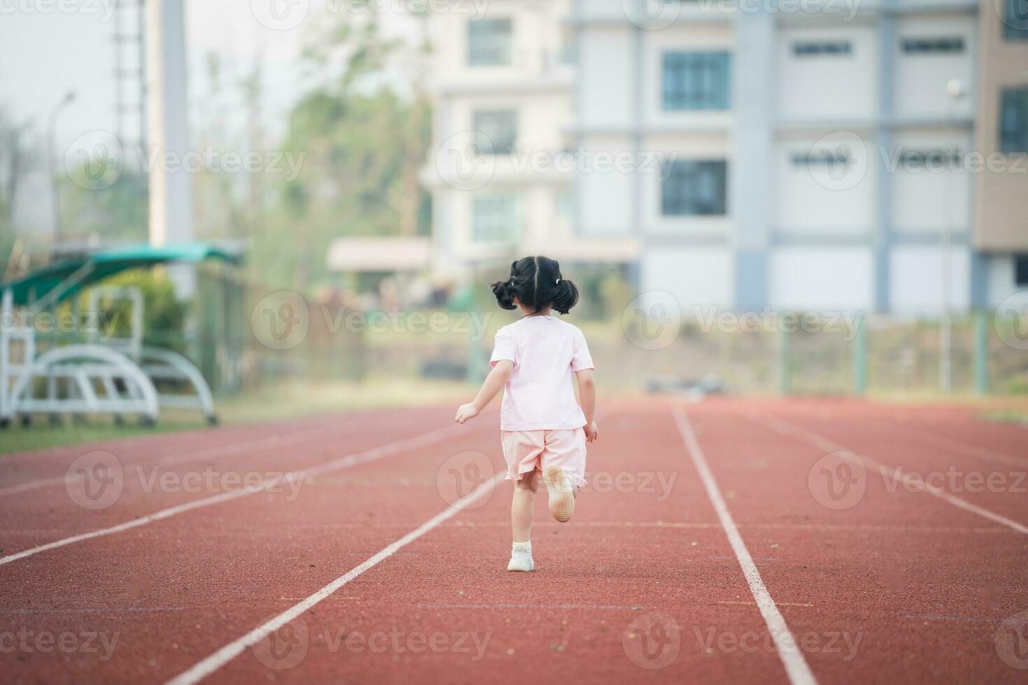 bebé asiático niña correr trotar a corriendo pista, correr campo a estadio. linda hembra ejercicio a puesta de sol contento bebé niña sonriendo a puesta de sol. linda bebé a corriendo pista. foto