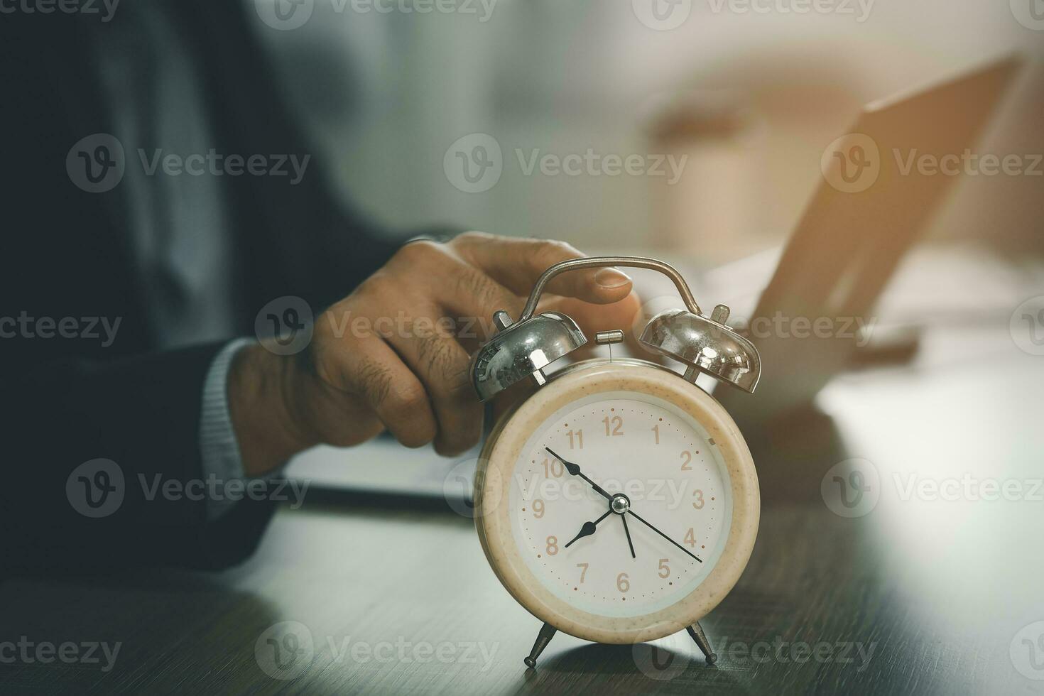 Selective focus of alarm clock on desk near business man using laptop to working overtime for deadline at home, concept of time management. business concept. photo