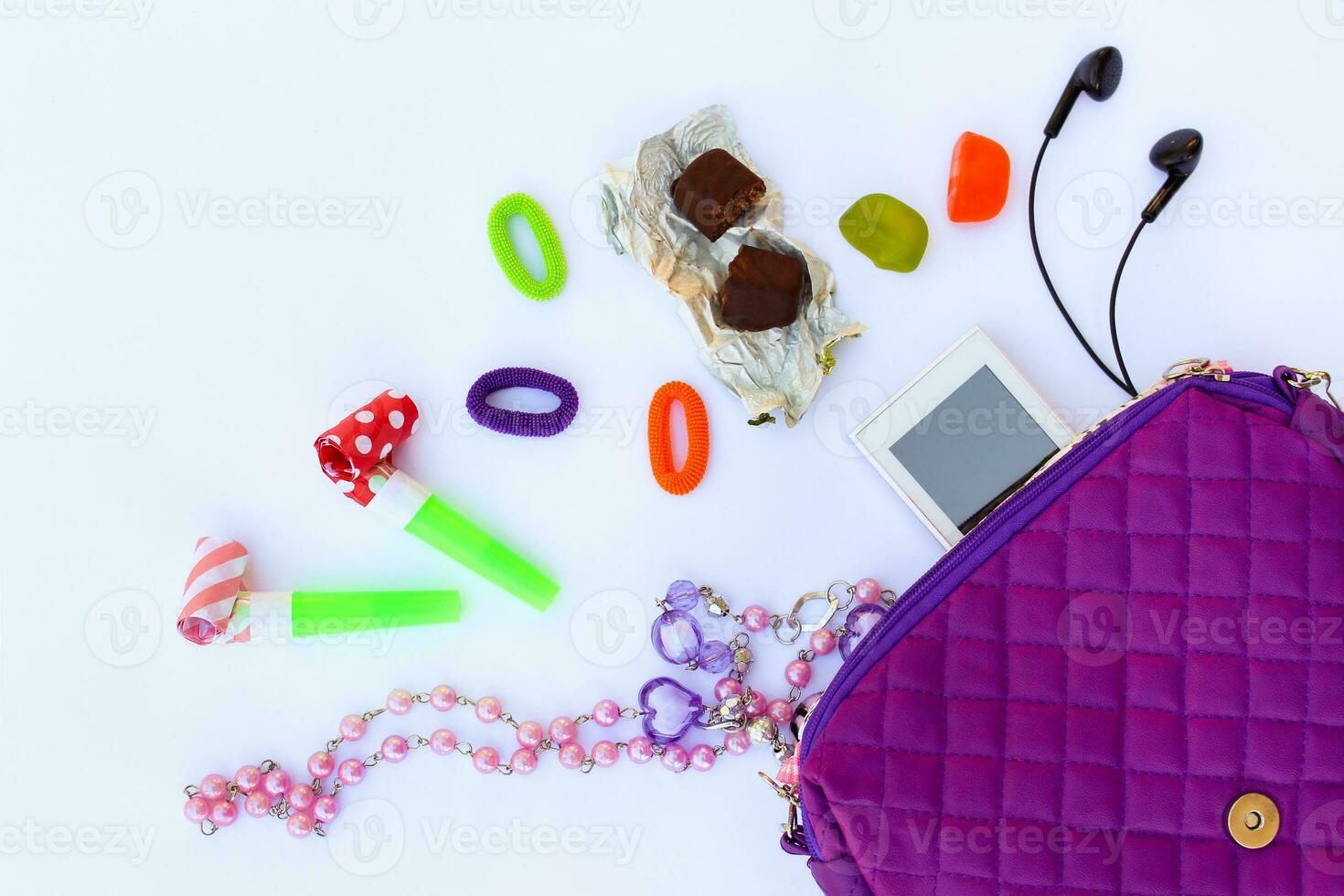 Children's handbag and accessories mobile phone, whistle, hair bands, candy, beads, headphones on white background. Top view. photo