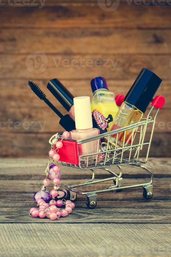 Shopping cart with cosmetics, beads on the old wood background. Toned image. photo