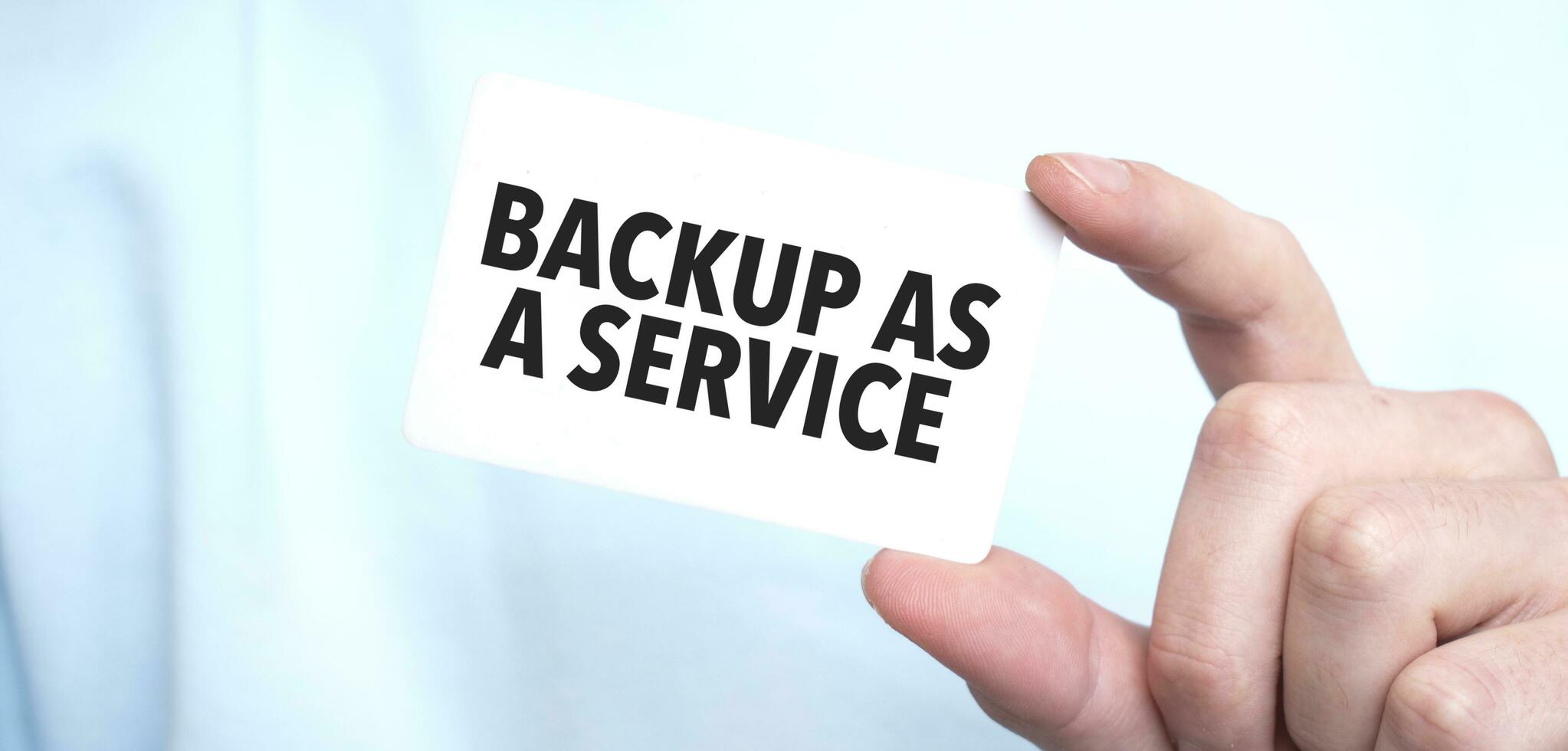 Man in blue sweatshirt holding a card with text BACKUP AS A SERVICE, business concept photo