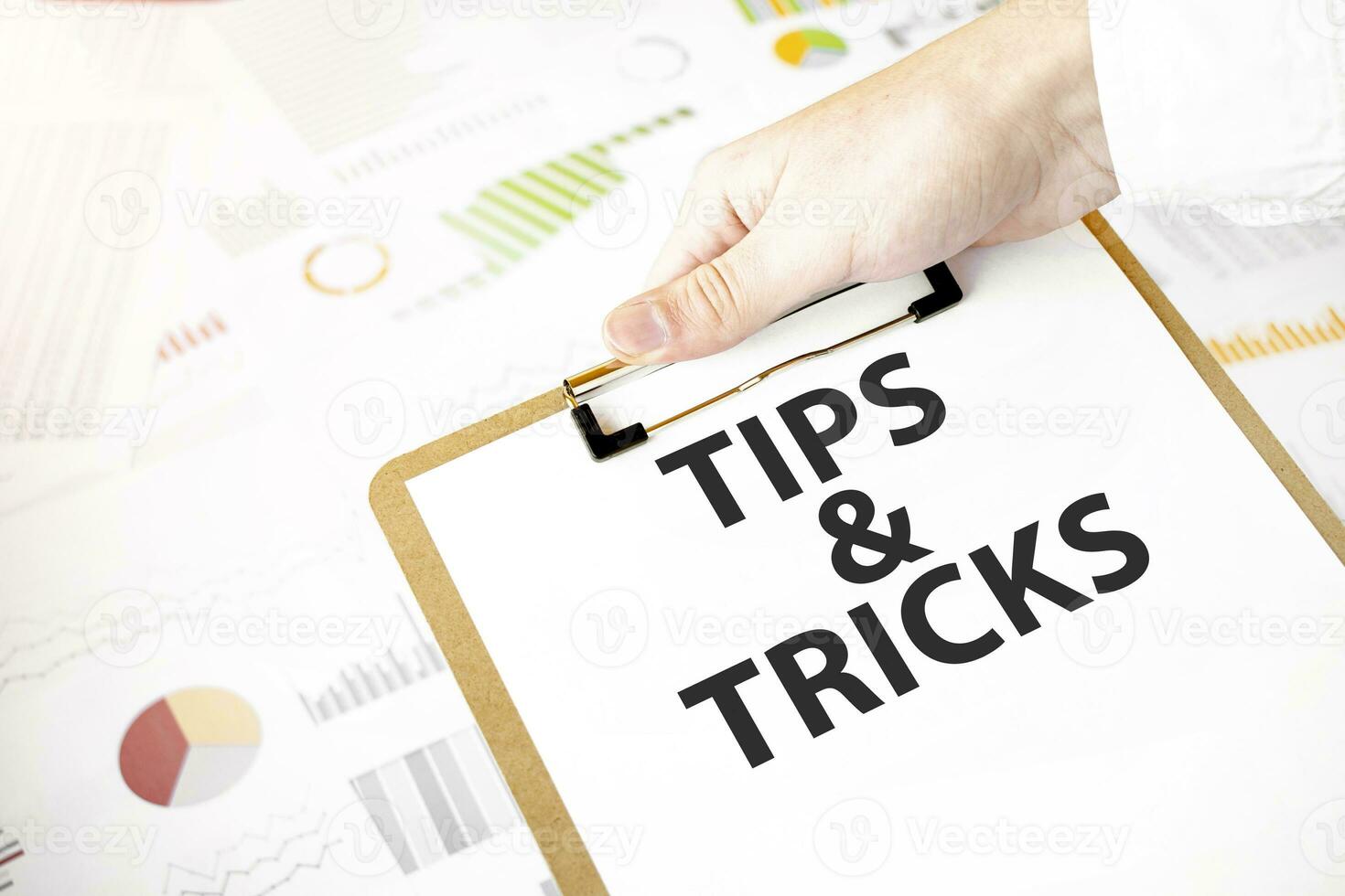 Text TIPS AND TRICKS on white paper plate in businessman hands with financial diagram. Business concept photo