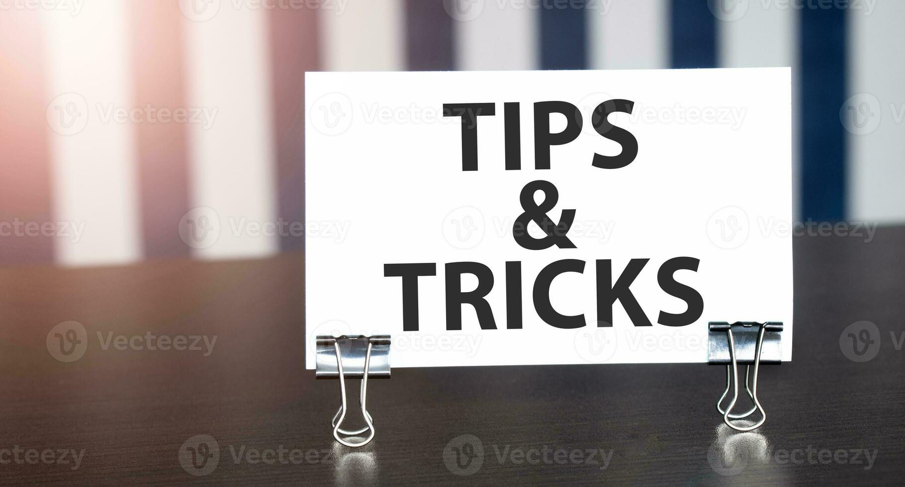 TIPS AND TRICKS sign on paper on dark desk in sunlight. Blue and white background photo