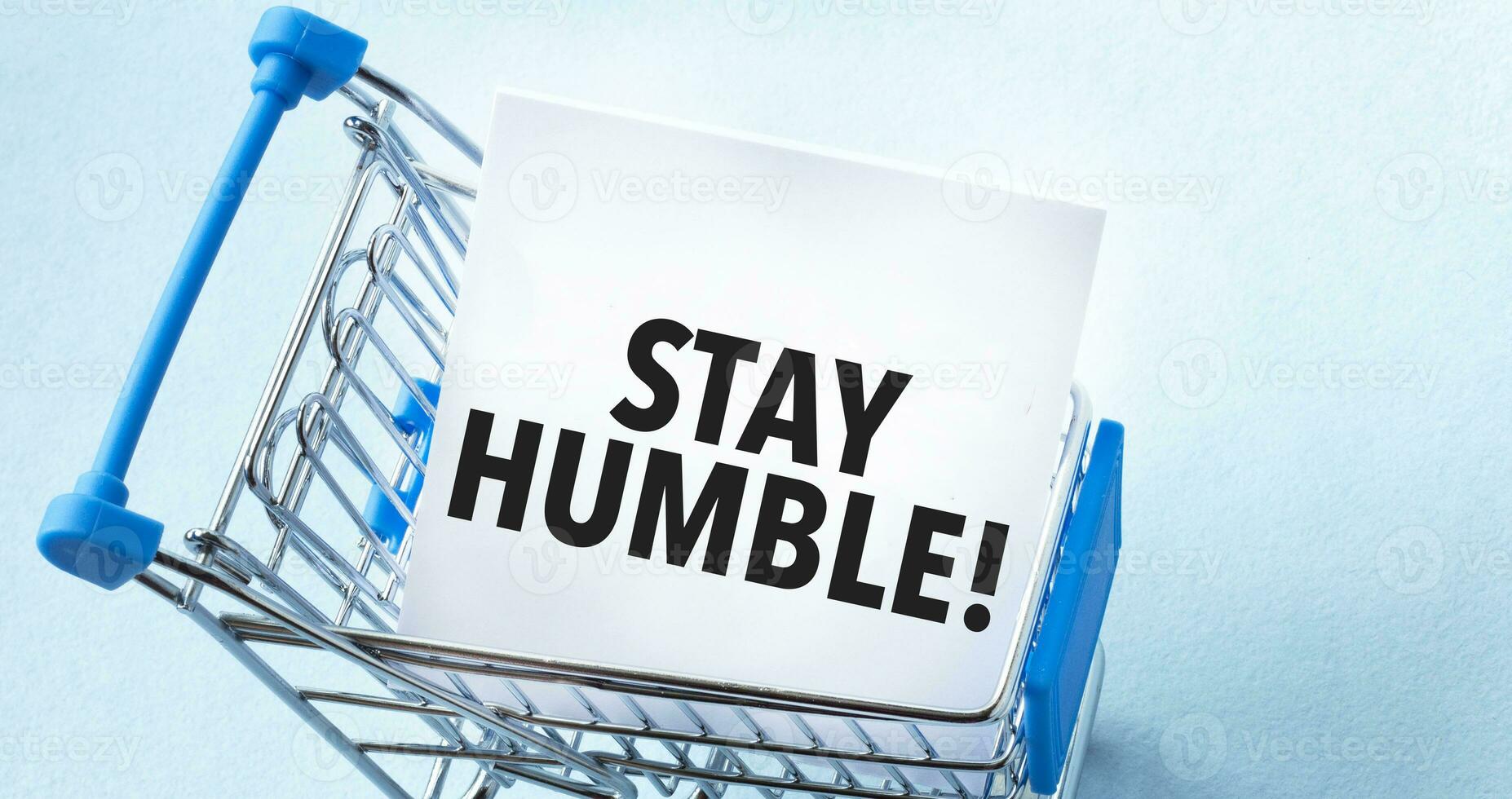 Shopping cart and text stay humble on white paper note list. Shopping list concept on blue background. photo