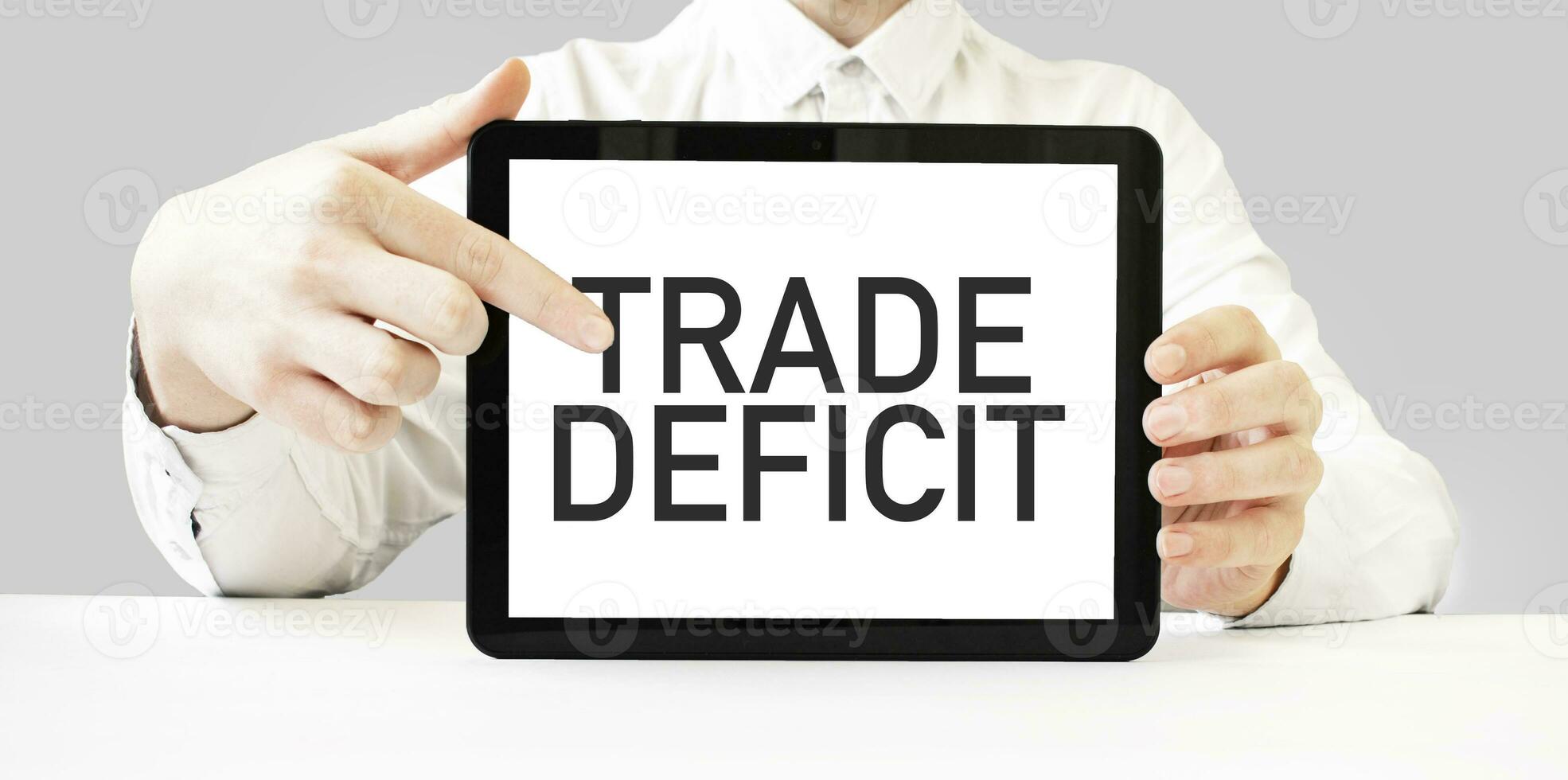 Text TRADE DEFICIT on tablet display in businessman hands on the white background. Business concept photo