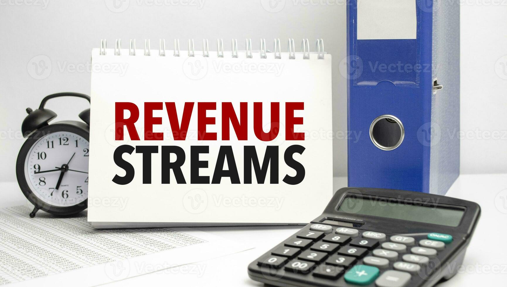 REVENUE STREAMS words on white notebook and calculator, black vintage alarm clock and blue paper folder photo