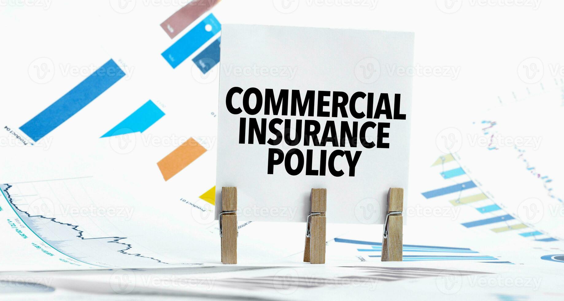 Text commercial insurance policy on paper sheet with chart, dice, spectacles, pen, laptop and blue and yellow push pin on wooden table photo