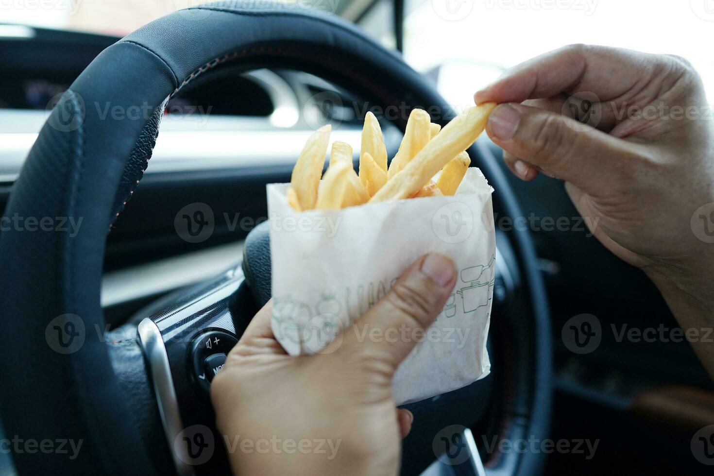 Asian woman driver hold and eat french fries in car, dangerous and risk an accident. photo