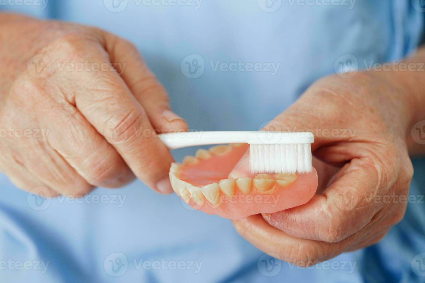 asiático mayor mujer paciente cepillo dientes dentadura con cepillo de dientes para masticar alimento. foto