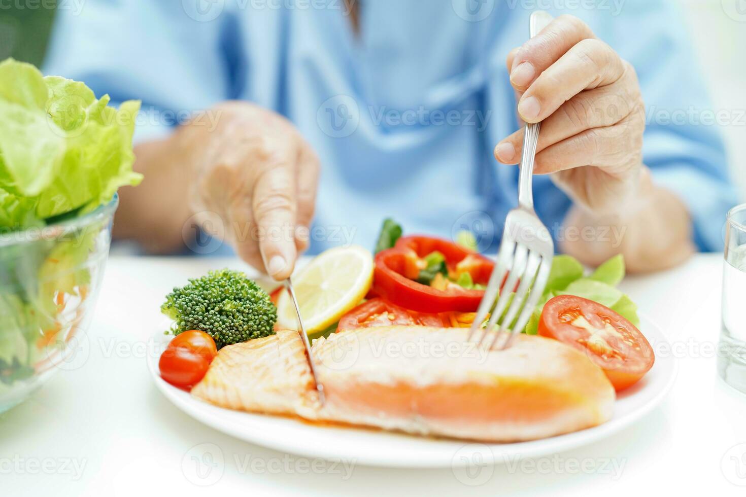 Asian elderly woman patient eating salmon stake and vegetable salad for healthy food in hospital. photo