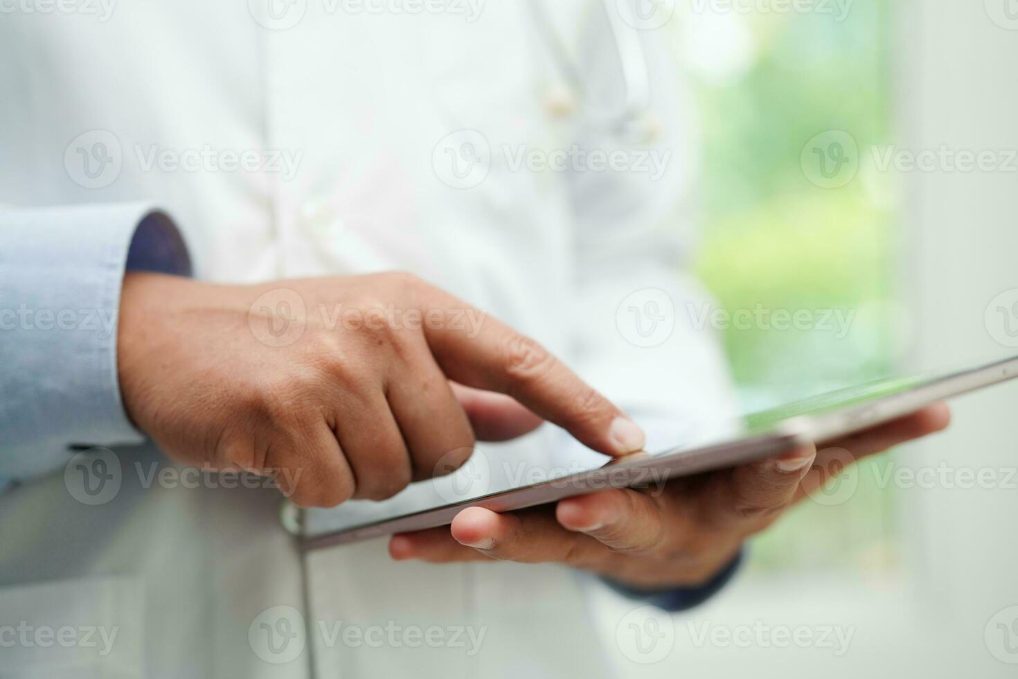 Asian man doctor using tablet computer to reading patient report, check up and search for solve treatment health medical online in hospital. photo