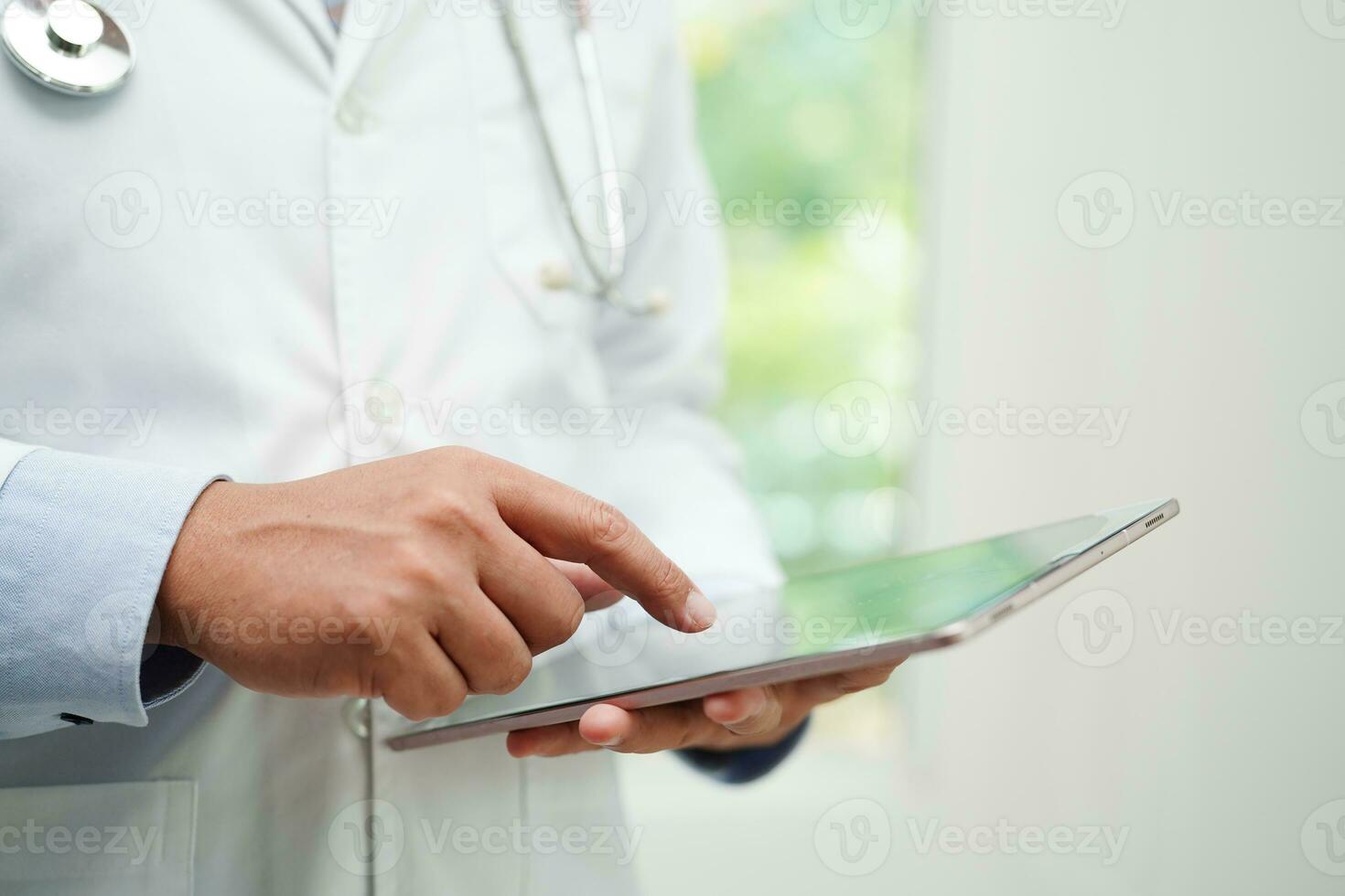 Asian man doctor using tablet computer to reading patient report, check up and search for solve treatment health medical online in hospital. photo