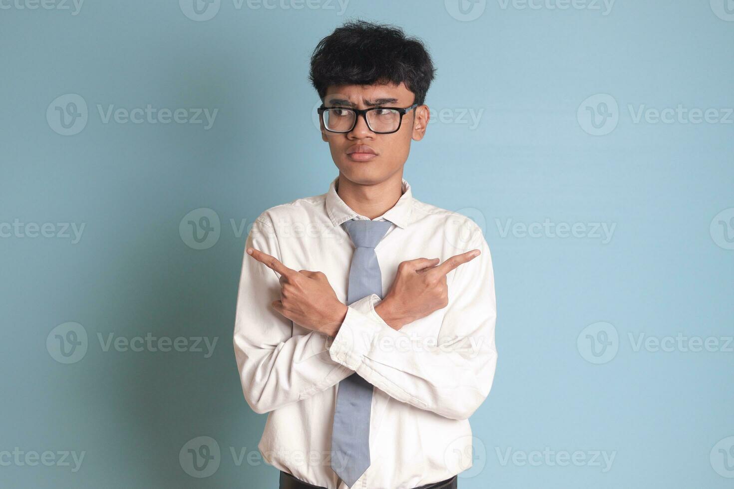 confuso mayor alto colegio estudiante vistiendo blanco camisa uniforme con gris Corbata con cruzado manos, señalando oblicuo, haciendo elección, elegir Entre dos opciones aislado imagen en azul antecedentes foto