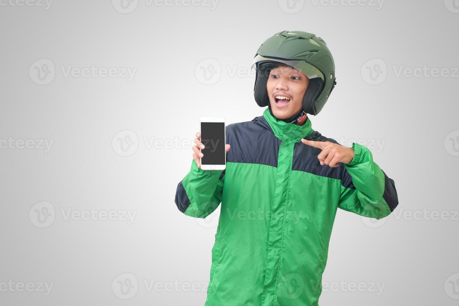 Portrait of Asian online taxi driver wearing green jacket and helmet showing and presenting blank screen mobile phone. Isolated image on white background photo