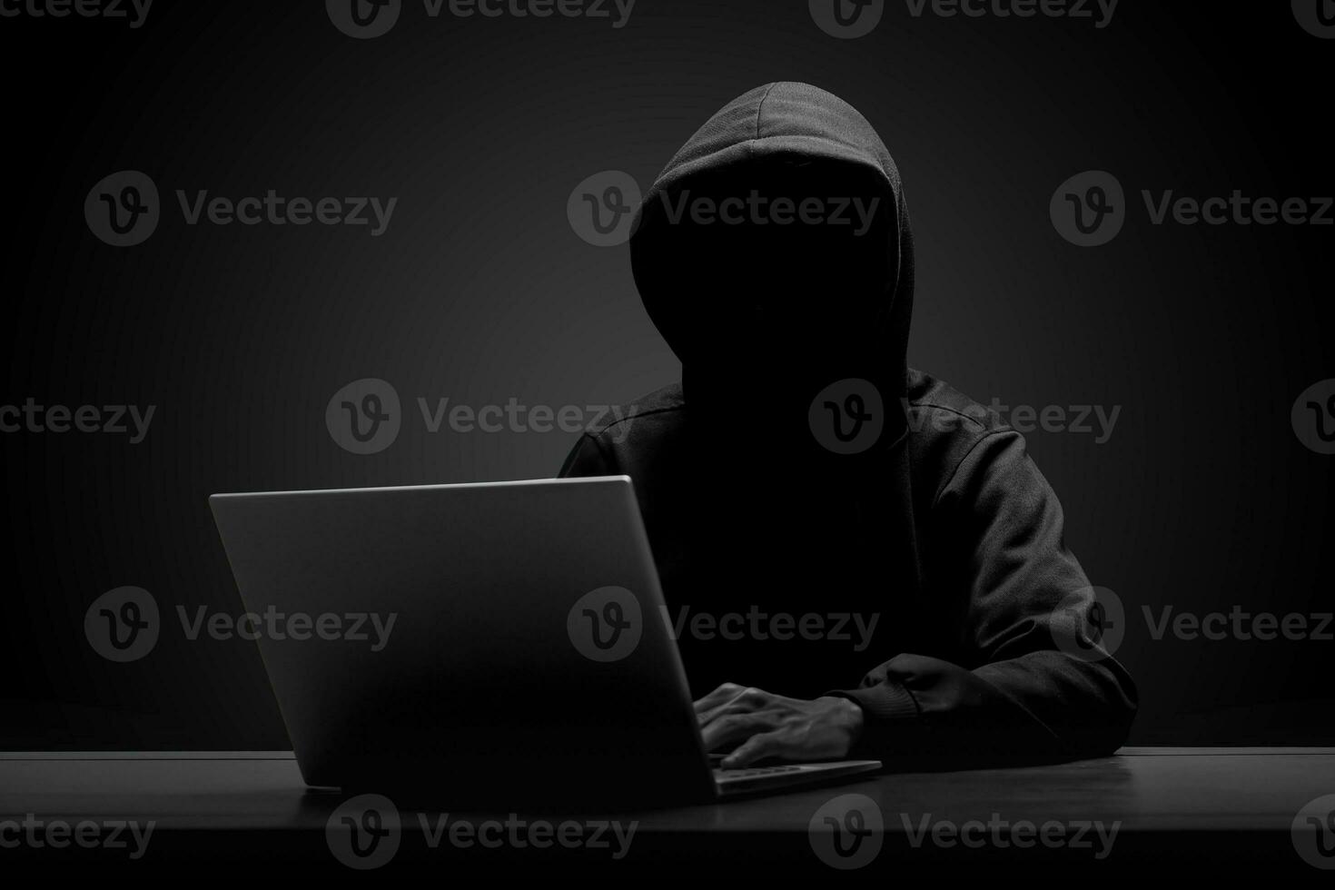 Mysterious man wearing black hoodie using laptop in the dark room. Hacker and cyber security concept. photo