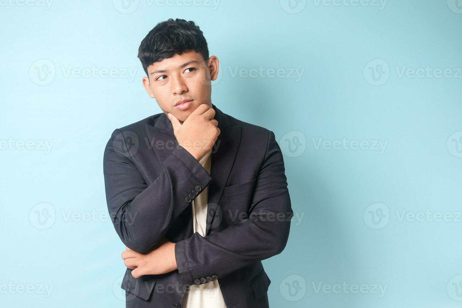 retrato de joven asiático negocio hombre en casual traje pensando difícil mientras mirando lejos. aislado imagen en azul antecedentes foto