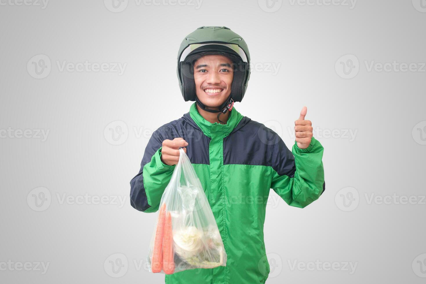 Portrait of Asian online taxi driver wearing green jacket and helmet delivering the vegetables from traditional market and pointing with finger. Isolated image on white background photo