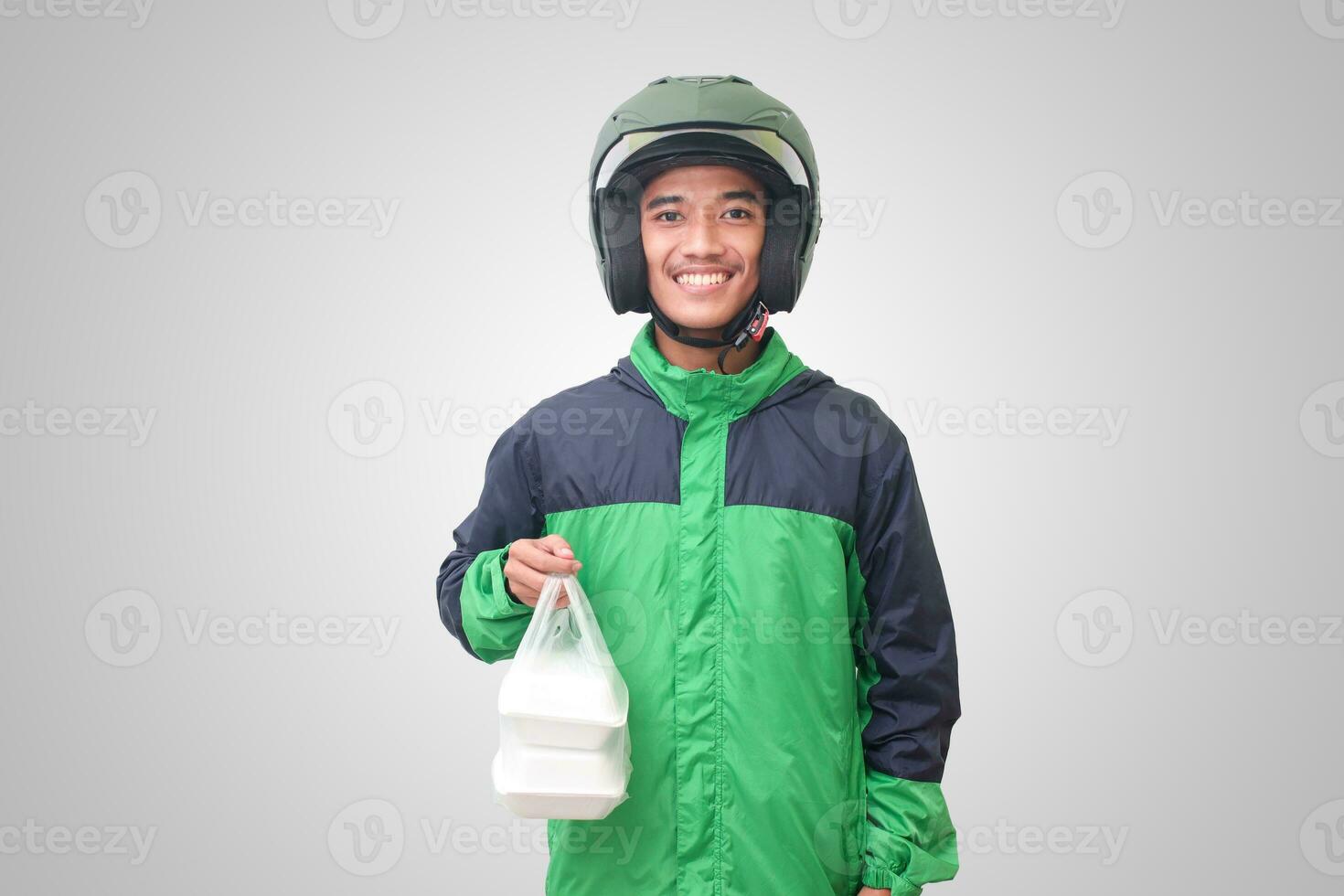 Portrait of Asian online taxi driver wearing green jacket and helmet holding food wrapped in foam plastic box. Isolated image on white background photo
